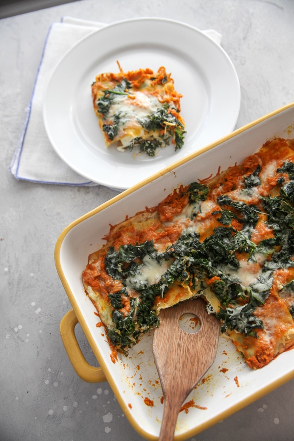 kale lasagna with a wooden spoon and serving on a white plate with napkin