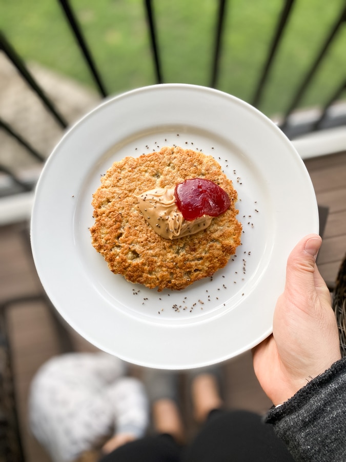 hand holding oatmeal pancake on a white plate with peanut butter and jelly