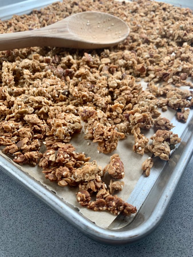 Crunchy Tahini Granola on stainless steel sheet pan with parchment paper and wooden spoon.