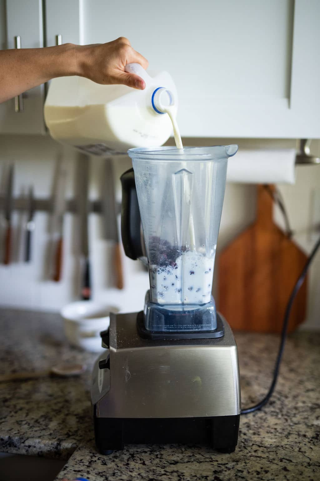 Pouring milk into a Vitamix blender with berries.