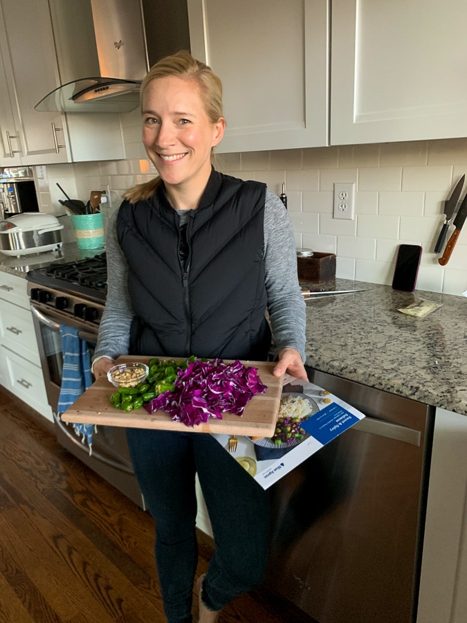 kath holding a cutting board and blue apron recipe card
