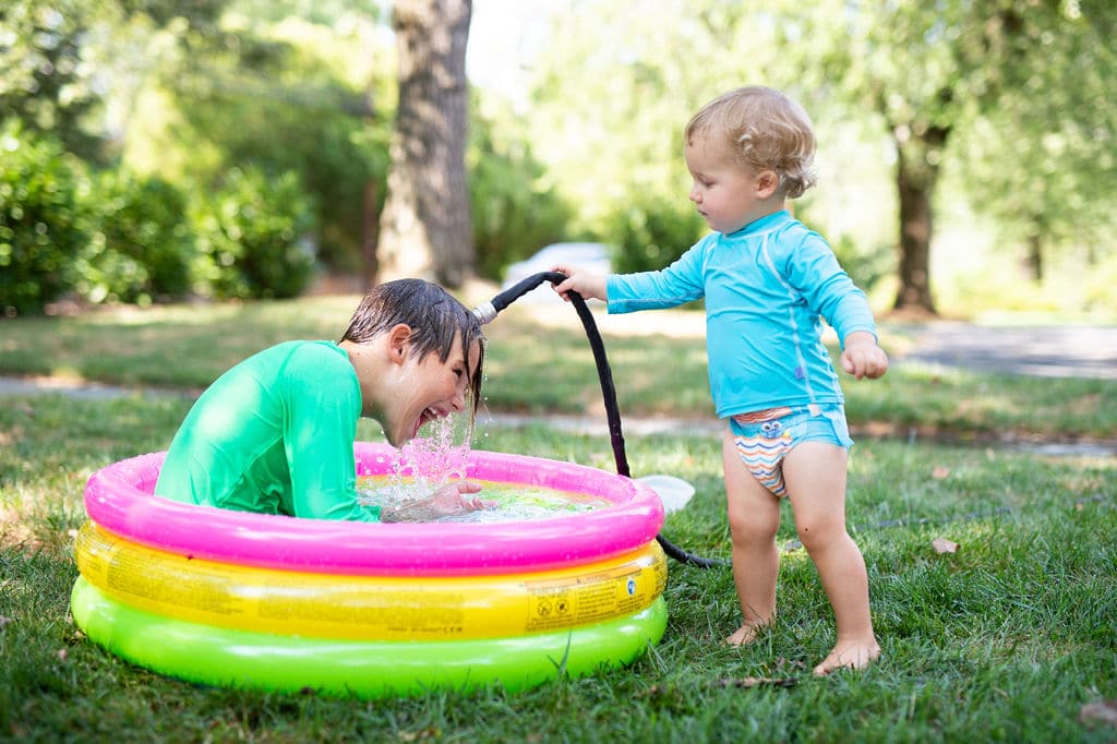 brothers in a kiddie pool with a hose