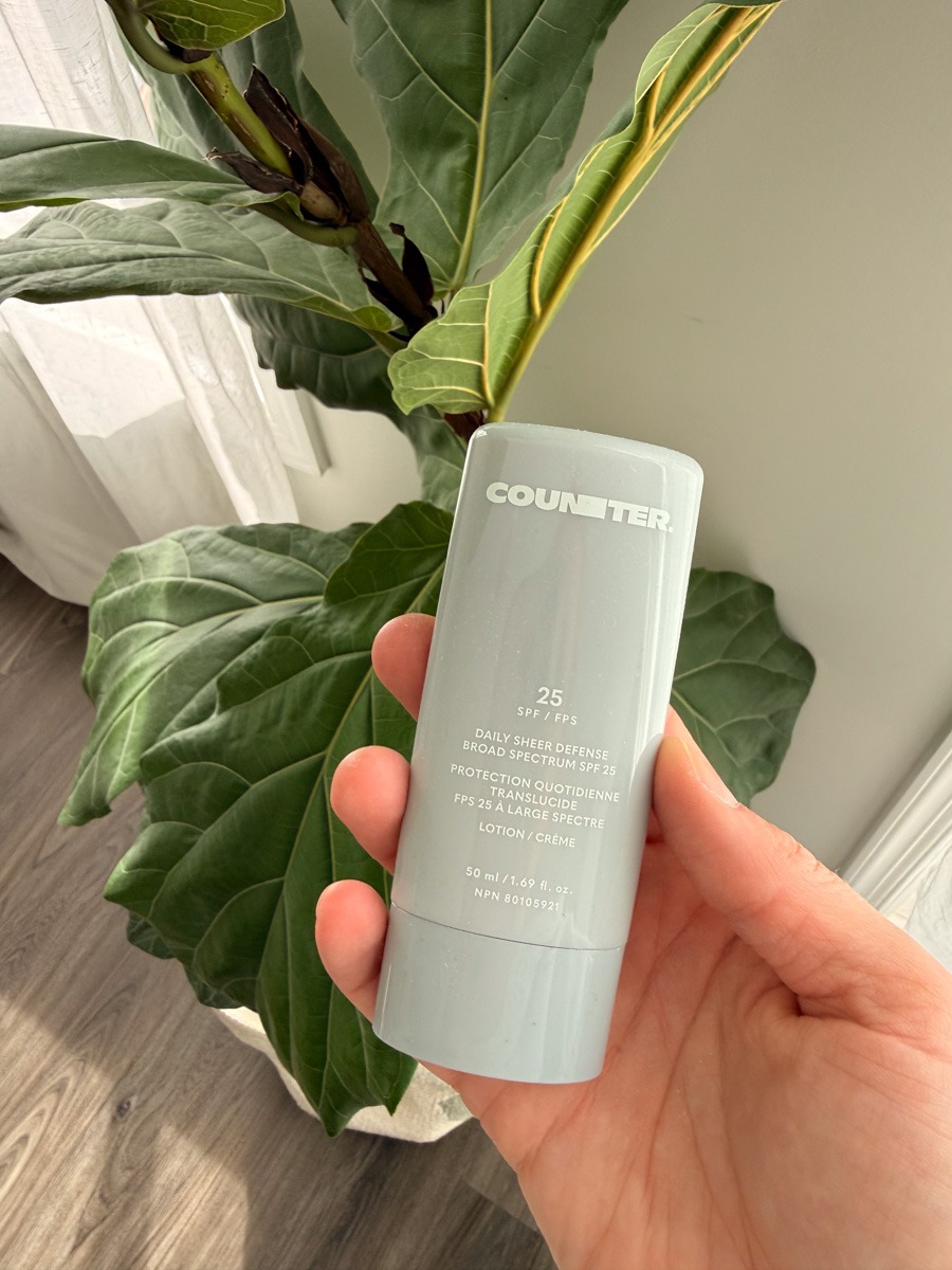 Counter Daily Sheer Defense Broad Spectrum SPF 25 sunscreen in hand with fig in back