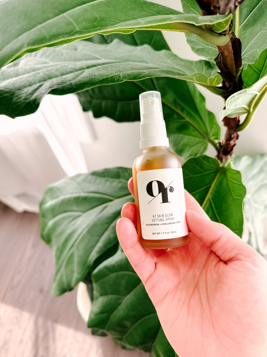 Olive Rose HT skin glow setting spray in a hand with a fiddle leaf fig